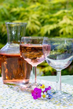 Şarap sürahisi ve soğuk gül şarabı ile bardaklar Yazın güneşli bir günde bahçede yabani çiçekler