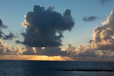 Deniz suyunun üzerinde dramatik bir gün batımı. Gri bulutlar ve güneş ışığı, doğa deniz manzarası.