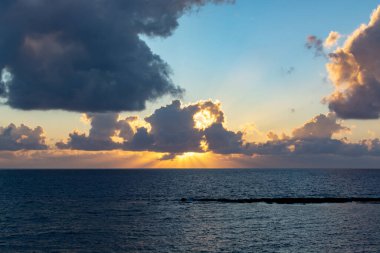 Deniz suyunun üzerinde dramatik bir gün batımı. Gri bulutlar ve güneş ışığı, doğa deniz manzarası.