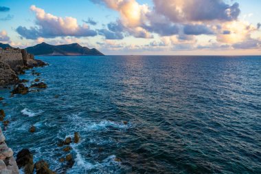 Deniz suyunun üzerinde dramatik bir gün batımı. Gri bulutlar ve güneş ışığı, doğa deniz manzarası.