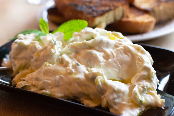 Tzatziki, cacik or tarator,  dip or sauce from Southeast Europe and Middle East made of salted strained yogurt mixed with cucumbers, garlic, salt, olive oil, vinegar or lemon juice, and dill, mint, parsley and thyme close up