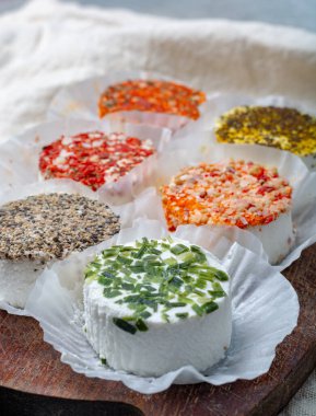 Fransız taze, yumuşak keçi peynirlerinin rengarenk çeşitleri farklı tat katar. Bitkiler, kırmızı biber, Hint körisi, bruscetta, soğan ve kurutulmuş domatesler. Kapatın.