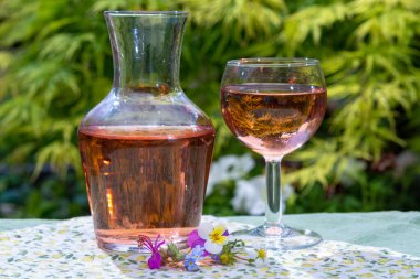 Şarap sürahisi ve cam, soğuk gül şarabı ve kır çiçekleri yazın güneşli bir günde bahçede.