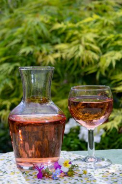 Şarap sürahisi ve cam, soğuk gül şarabı ve kır çiçekleri yazın güneşli bir günde bahçede.
