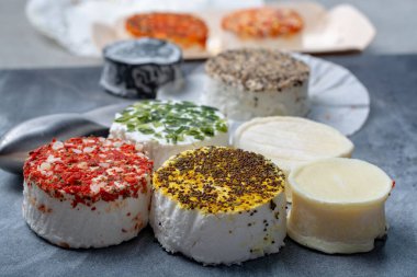 Fransız taze, yumuşak keçi peynirlerinin rengarenk çeşitleri farklı tat katar. Bitkiler, kırmızı biber, Hint körisi, bruscetta, soğan ve kurutulmuş domatesler. Kapatın.