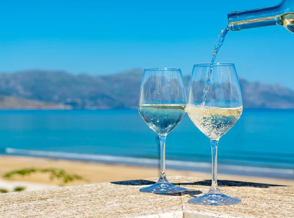 Waiter pouring white wine in wine glasses on outdoor terrace witn blue sea and mountains view on background in sunny day