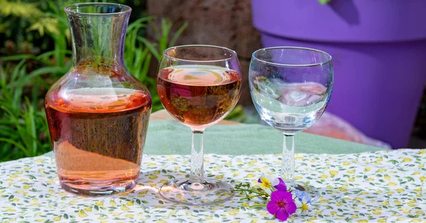 Wine carafe and glasses with cold rose wine and wild flowers in summer sunny day in garden