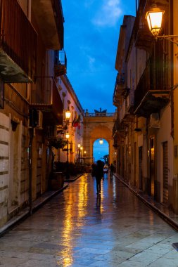 Gece Marsala 'da eski bir cadde yağmur altında sokak lambalarının yansımasıyla, Sicilya, İtalya
