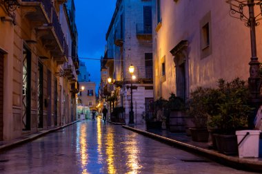 Gece Marsala 'da eski bir cadde yağmur altında sokak lambalarının yansımasıyla, Sicilya, İtalya