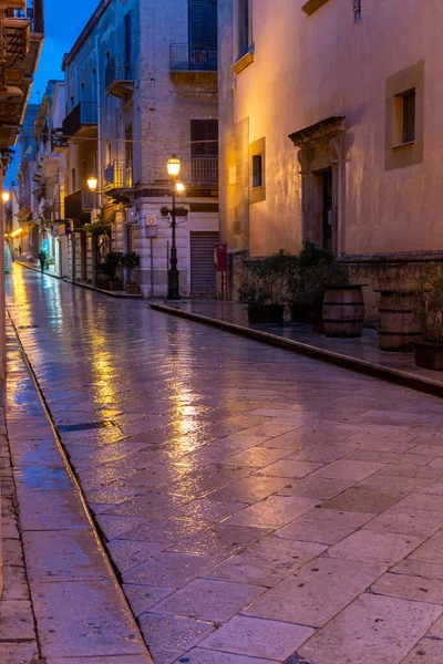 Old street in Marsala at night in rain with reflection of street lights, Sicily, Italy