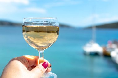 Balkonda servis edilen beyaz şaraplı el ve deniz manzaralı yakın çekim.