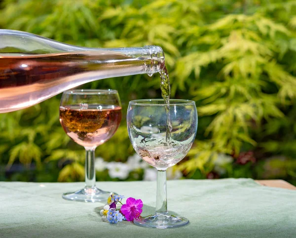 Waiter pouring cold rose wine in glasses in summer sunny day in blossoming garden close up