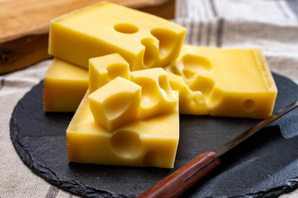 Block of Swiss medium-hard yellow cheese emmental or emmentaler with round holes and cheese knife close up