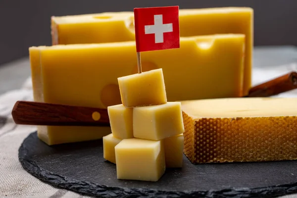 Swiss cheeses, block of medium-hard yellow cheese emmental or emmentaler with round holes and matured gruyere close up served in cubes as mountain top with Swiss flag.