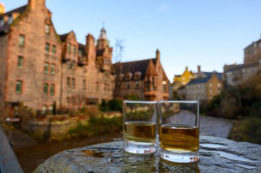 Scotch single malts or blended whisky spirits in glasses with old houses of Edinburgh city on background, Scotland, UK clipart