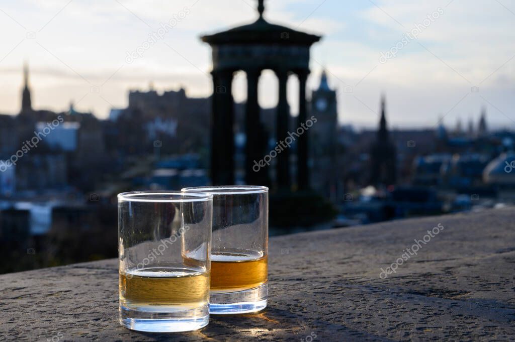 Scotch single malts or blended whisky spirits in glasses with Calton hill in Edinburgh on background, Scotland, UK
