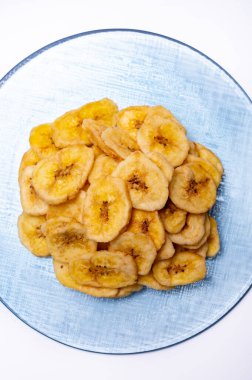 Sağlıklı tatlı atıştırmalık, beyaz arka planda geri dönüştürülmüş cam tabakta gevrek susuz kalmış şekersiz muz cipsi.