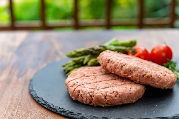 Ingredients for tasty vegan dinner, meat free plants based steak, green asparagus and red tomatoes close up