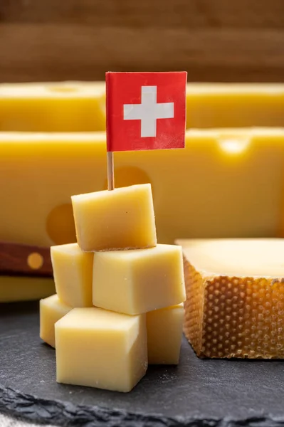 Swiss cheeses, block of medium-hard yellow cheese emmental or emmentaler with round holes and matured gruyere close up served in cubes as mountain top with Swiss flag.
