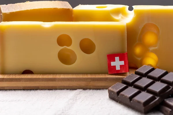 Tasty Swiss food, block of medium-hard yellow cheese emmental or emmentaler with round holes and high quality milk chocolate close up