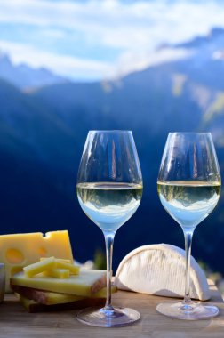 Fransa 'nın Savoy bölgesinden lezzetli peynir ve şarap, Beaufort, abondance, emmental, tomme ve reblochon de savoie peynirleri ve yazın açık havada sunulan beyaz şarap arka planda Alp dağlarının zirveleri
