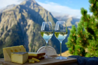 Fransa 'nın Savoy bölgesinden lezzetli peynir ve şarap, Beaufort, abondance, emmental, tomme ve reblochon de savoie peynirleri ve yazın açık havada sunulan beyaz şarap arka planda Alp dağlarının zirveleri