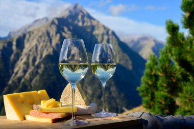 Fransa 'nın Savoy bölgesinden lezzetli peynir ve şarap, Beaufort, abondance, emmental, tomme ve reblochon de savoie peynirleri ve yazın açık havada sunulan beyaz şarap arka planda Alp dağlarının zirveleri