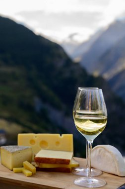 Fransa 'nın Savoy bölgesinden lezzetli peynir ve şarap, Beaufort, abondance, emmental, tomme ve reblochon de savoie peynirleri ve yazın açık havada sunulan beyaz şarap arka planda Alp dağlarının zirveleri