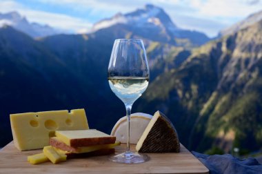 Fransa 'nın Savoy bölgesinden lezzetli peynir ve şarap, Beaufort, abondance, emmental, tomme ve reblochon de savoie peynirleri ve yazın açık havada sunulan beyaz şarap arka planda Alp dağlarının zirveleri