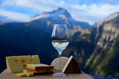 Fransa 'nın Savoy bölgesinden lezzetli peynir ve şarap, Beaufort, abondance, emmental, tomme ve reblochon de savoie peynirleri ve yazın açık havada sunulan beyaz şarap arka planda Alp dağlarının zirveleri