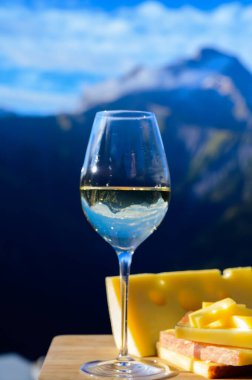Fransa 'nın Savoy bölgesinden lezzetli peynir ve şarap, Beaufort, abondance, emmental, tomme ve reblochon de savoie peynirleri ve yazın açık havada sunulan beyaz şarap arka planda Alp dağlarının zirveleri