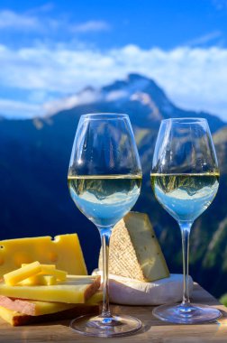 Fransa 'nın Savoy bölgesinden lezzetli peynir ve şarap, Beaufort, abondance, emmental, tomme ve reblochon de savoie peynirleri ve yazın açık havada sunulan beyaz şarap arka planda Alp dağlarının zirveleri