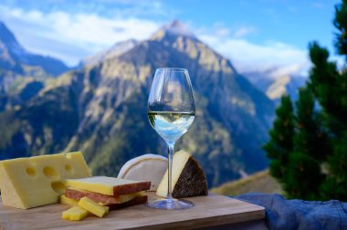 Fransa 'nın Savoy bölgesinden lezzetli peynir ve şarap, Beaufort, abondance, emmental, tomme ve reblochon de savoie peynirleri ve yazın açık havada sunulan beyaz şarap arka planda Alp dağlarının zirveleri