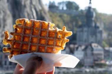 Hand holding sweet fresh baked Belgian waffles served outdoor with view on Maas river in Dinant, Wallonia, Belgium close up clipart