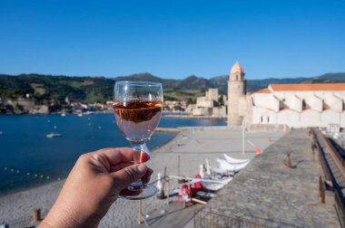 Güneş ışığında bir bardak gül Collioure AOC şarabı, Collioure kasabası manzaralı, renkli evler, kilise, kale ve plajlar, Occitanie, Fransa, turist beldesi