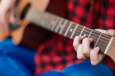 Kahverengi bir klasik akustik gitarın yakın çekimi, telleri çalan bir bayan müzisyenin eliyle. Bulanık doğal bir arkaplan üzerine yakın çekim yapan bir kişinin ellerinde telli müzik aleti.