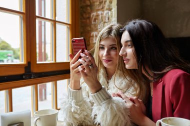 İki mutlu genç kızla kafede kahve içme smartphone. Teknoloji, yaşam biçimi ve insanlar kavramı -