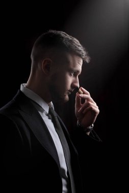 Smokin şık genç moda adam. Puro kokluyor. Tat puro. Siyah arka plan üzerine.