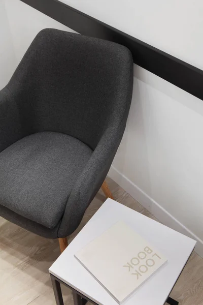Серый кресло и минималистичный стол белый и черный с металлическим конструкцием.Книга на столе с образцом text.Concept — стоковое фото