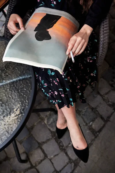 Primer plano de hermosa chica con papel de noticias y cigarrillo en la mano sentado cerca de la mesa . — Foto de Stock