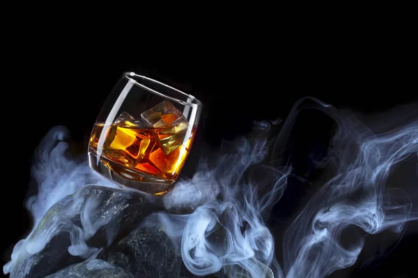 Glass of whiskey with ice .Creative photo glass of whiskey on stone with fog and black background.Copy space.Advertising shot — Stock Photo, Image