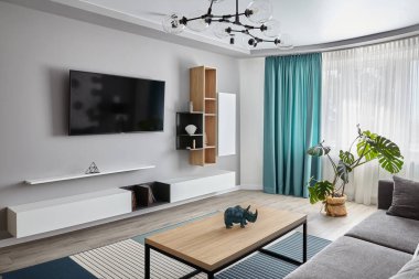 Modern oturma odası. Gri kanepe, halı ve perdeler. Modern zemin lambası. Tahta kahve masası. Beyaz Cyan renkleri.