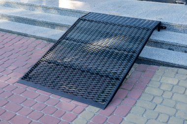 Siyah metal bir rampa, şehir ortamında hareket güçlüğü çeken bireylere erişim olanağı sağlayan bir merdivene dayanır..