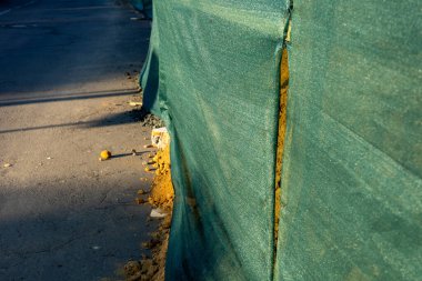 Yeşil örgülü çit, bir inşaat alanını çevreleyerek gün batımında aydınlanan yoldaki toprak yığınını ortaya çıkarıyor..