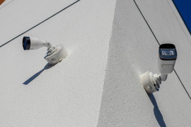 Bir binanın köşesine yerleştirilmiş iki güvenlik kamerası temiz bir gökyüzü ve parlak bir çevrede gözetleme alanı sağlıyor..