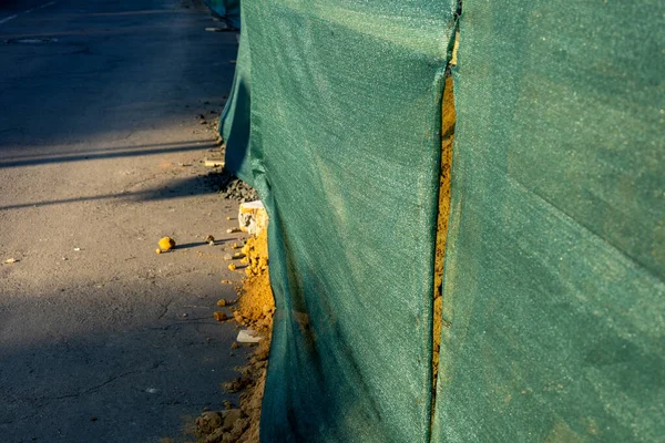 Yeşil örgülü çit, bir inşaat alanını çevreleyerek gün batımında aydınlanan yoldaki toprak yığınını ortaya çıkarıyor..