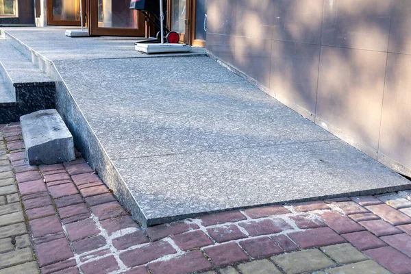 Pürüzsüz, erişilebilir bir rampa, tuğladan bir yolu bir kamu binasının dışındaki beton bir zemine bağlar ve tüm bireylerin erişimini kolaylaştırır..