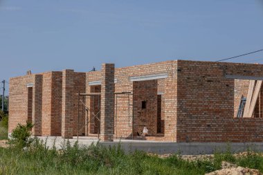 Güneşli bir günde inşaat halindeki tamamlanmamış tuğla ev duvarları. Beton temeli ve yeşil çimenli yeni konut projesi.