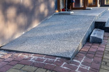 Gri benekli taş rampa bina girişine erişim sağlıyor. Kırmızı tuğla kaldırım, karanlık basamaklar ve duvar. Açık hava mimari tasarımı.