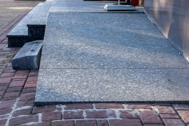 Kalıplı gri granit levhalar kırmızı tuğla kaldırıma bağlanıyor. Taş basamaklar açık bir şehir yoluna çıkıyor. Dayanıklı modern malzeme yüzey ayrıntıları.